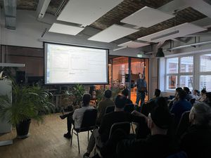 Photo of the Elixir meetup 100th edition, bitcrowd Founder in front of a large screen giving a talk to many seated people